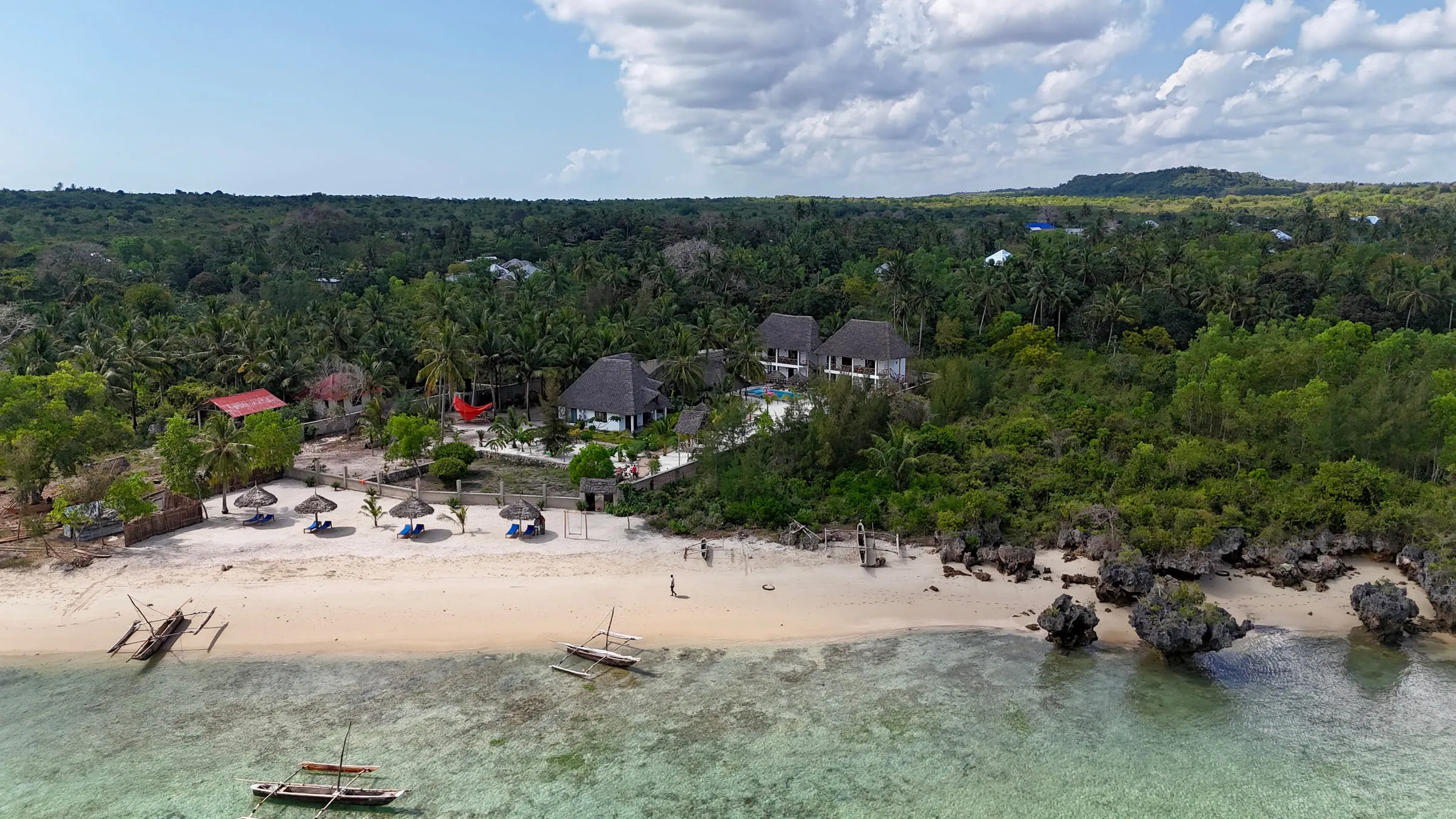 Aerial view of the Pamoja Villas coastline, thatched roofs set back from a pale sand beach and turquoise reef