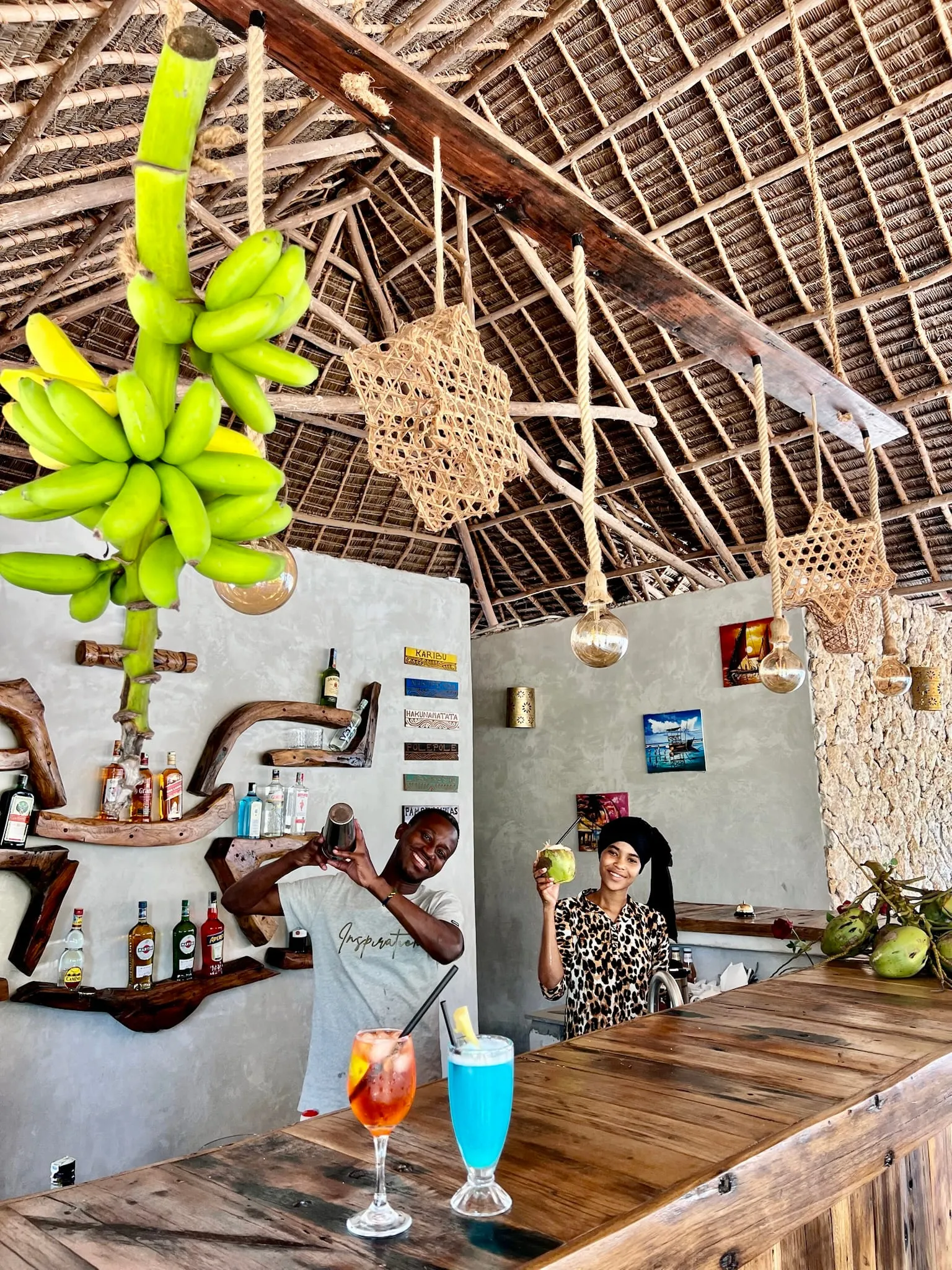 Two cocktails on the timber bar under the makuti roof with bunches of bananas hanging above