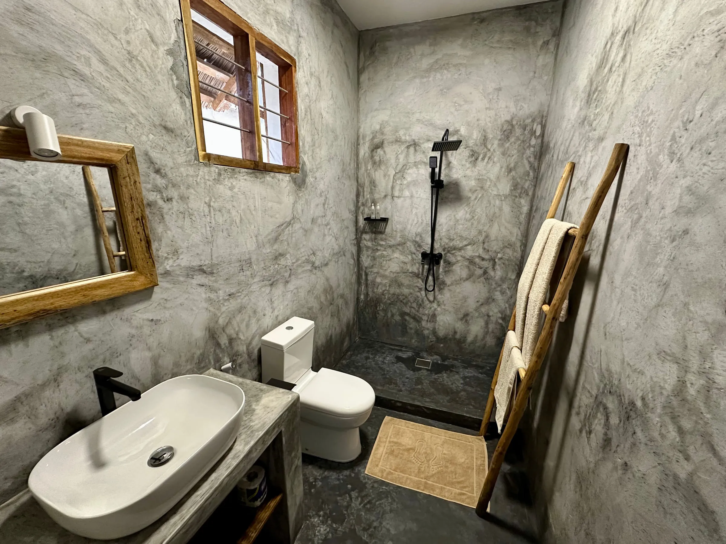 Polished concrete bathroom with a driftwood-framed mirror and open walk-in shower