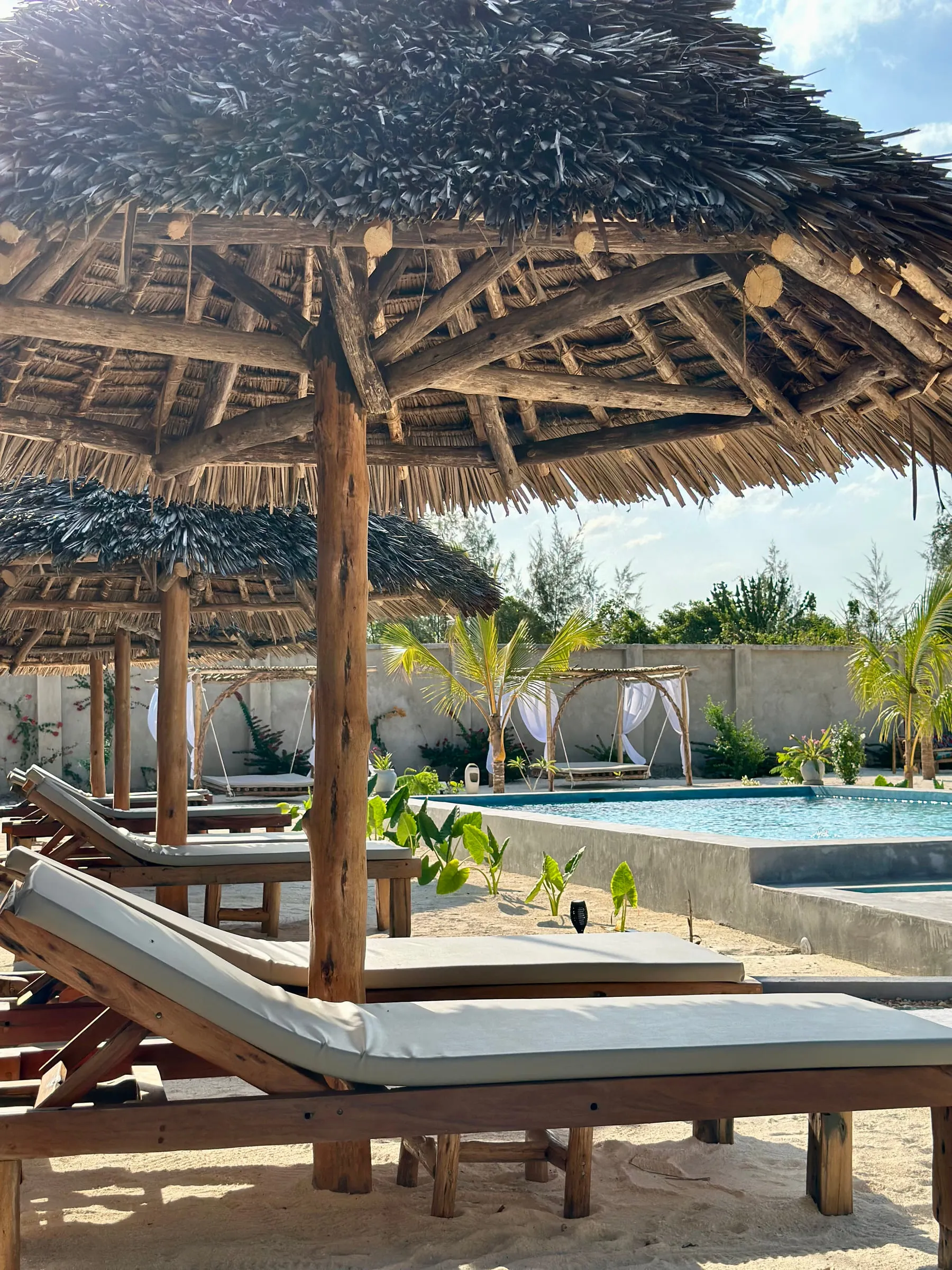 A cushioned wooden day bed under a thatched umbrella at the edge of the pool