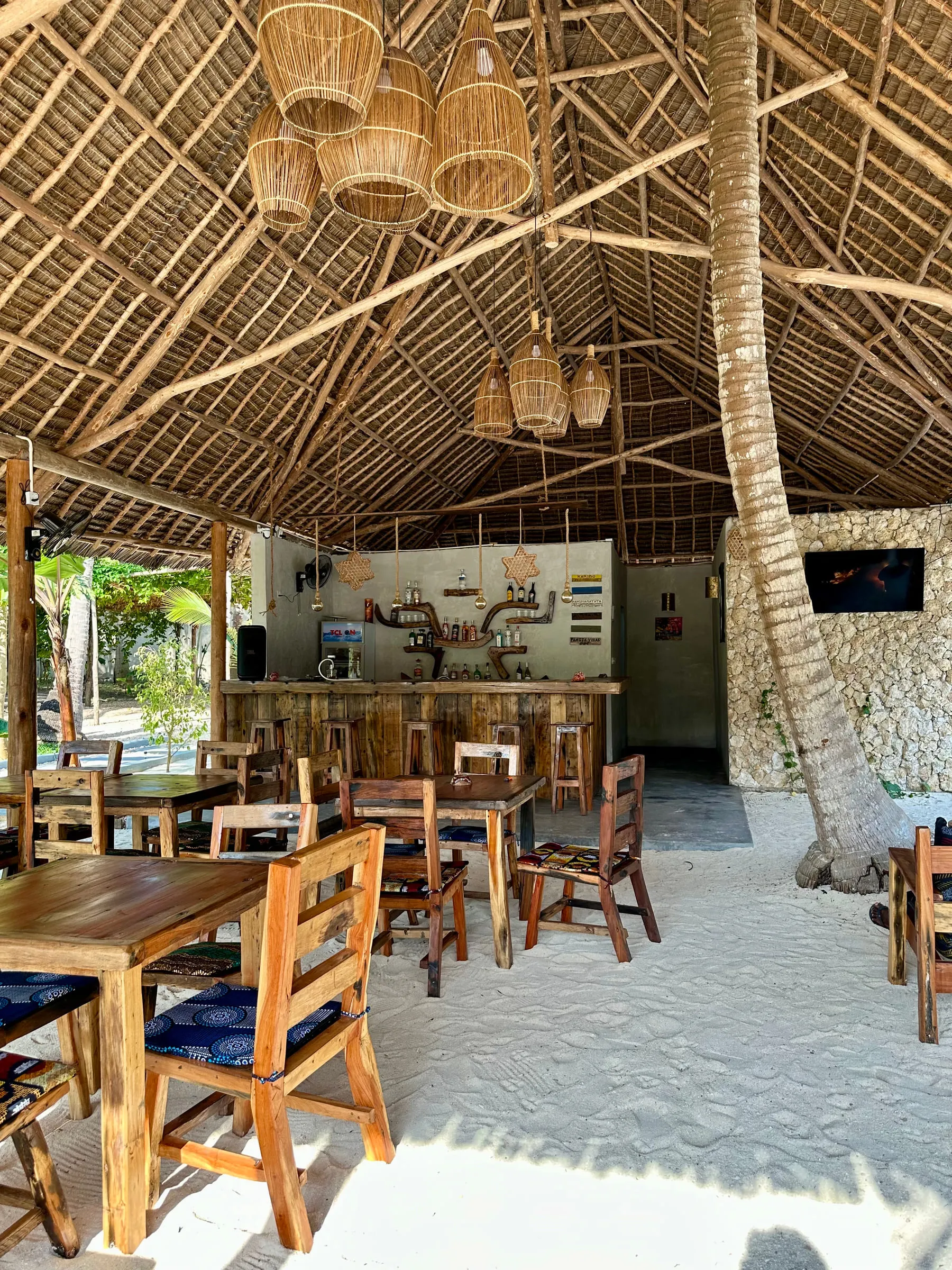 Inside the dining pavilion looking out to the garden, with timber tables and woven pendant lights