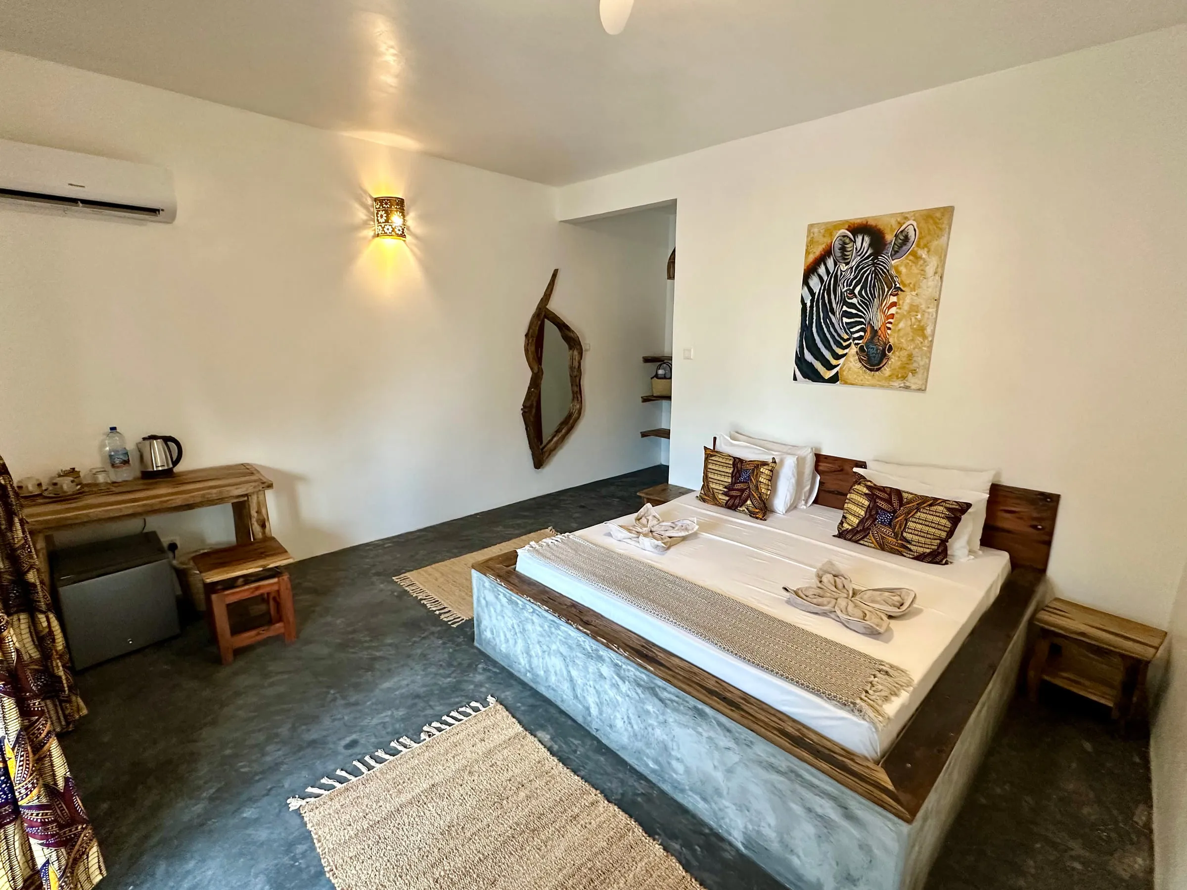King bed in white linen beneath a framed zebra print with warm wall lights either side