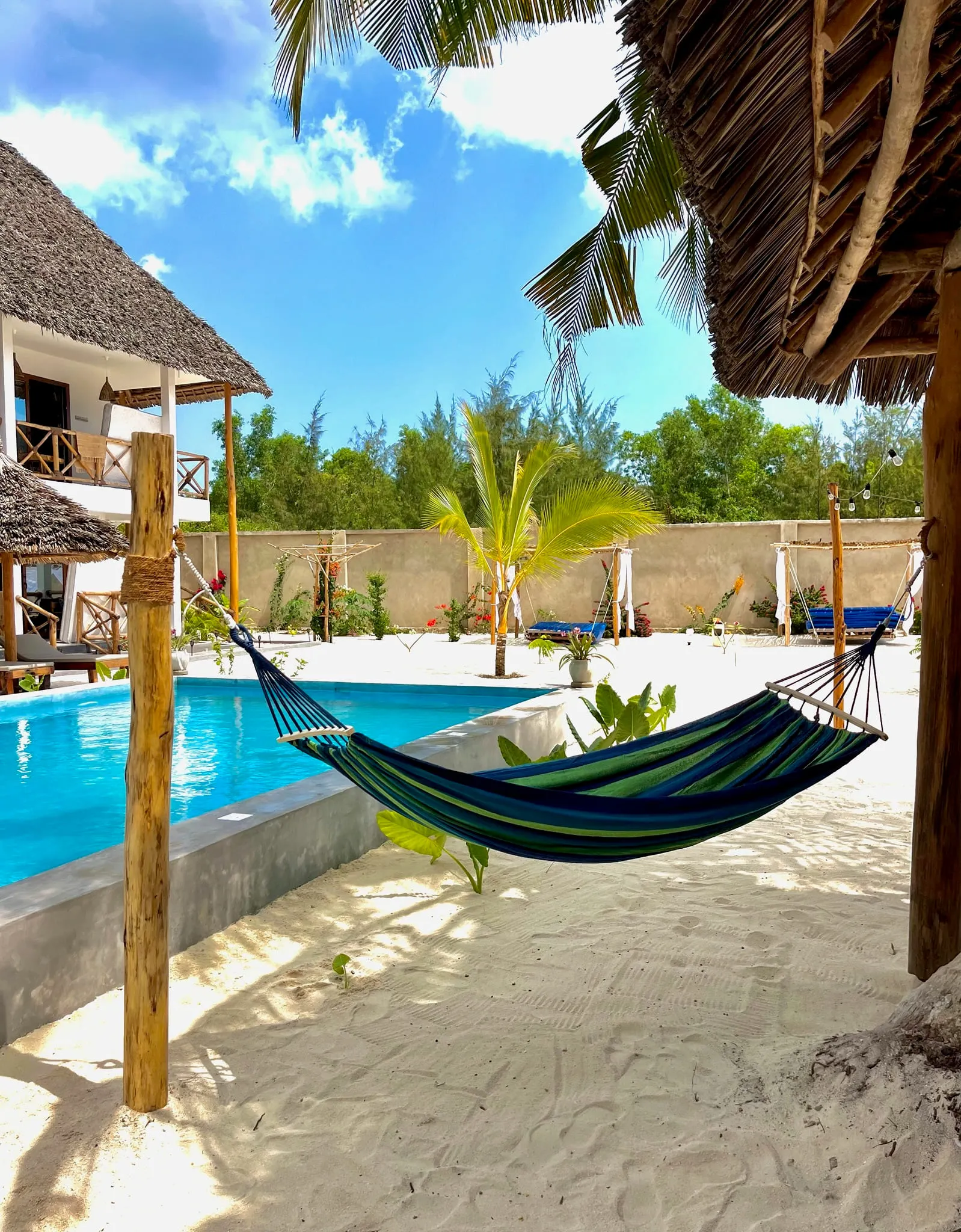 A striped hammock hanging beside the pool between white columns and palm trees