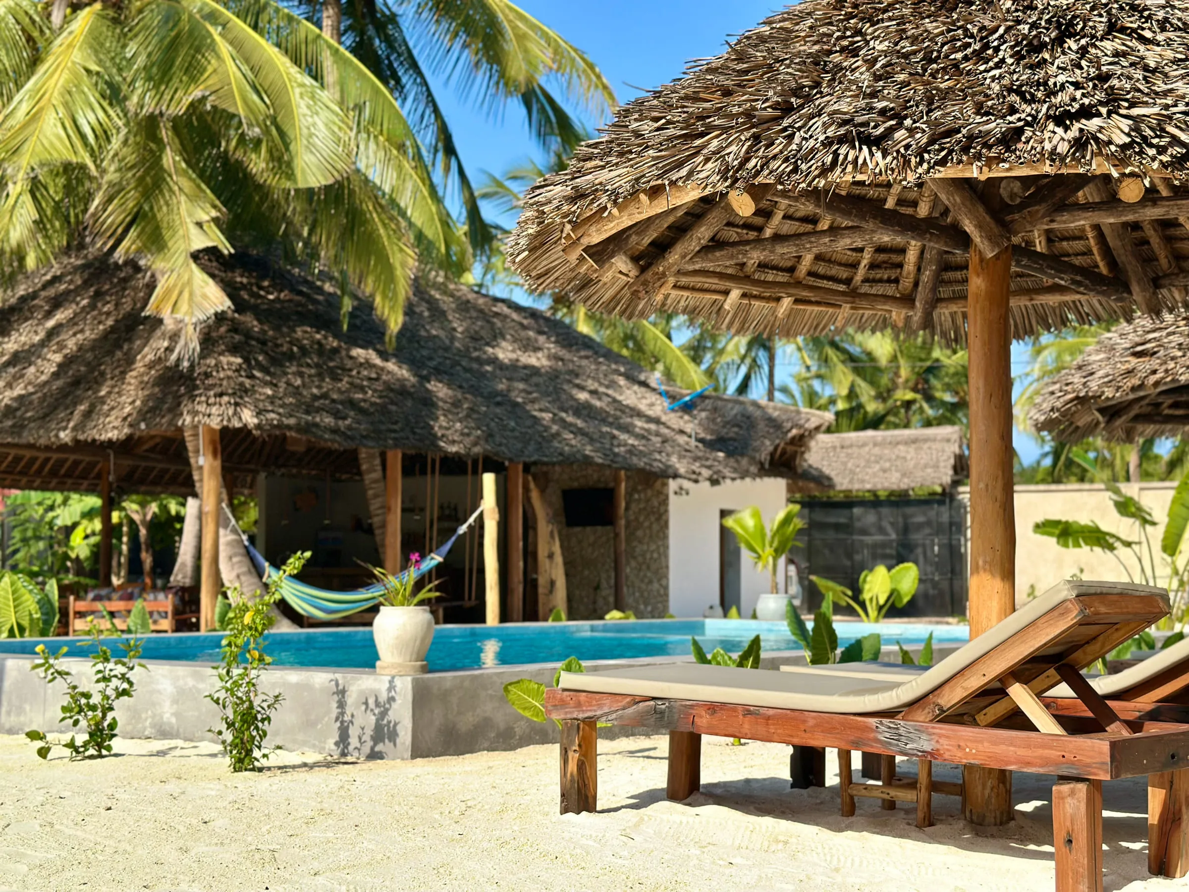 A hammock and day beds under a makuti roof looking out towards the pool