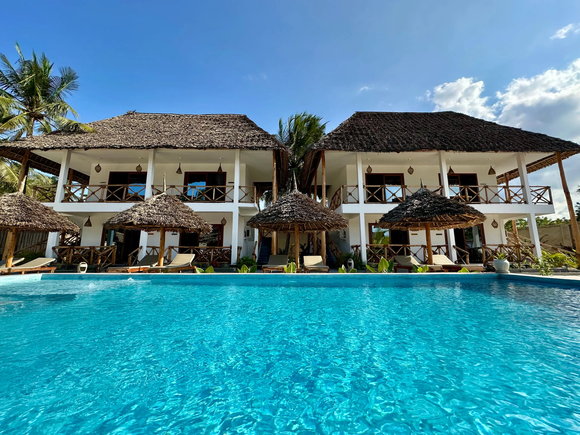 The swimming pool at Pamoja Villas with the whitewashed, thatched villa buildings behind