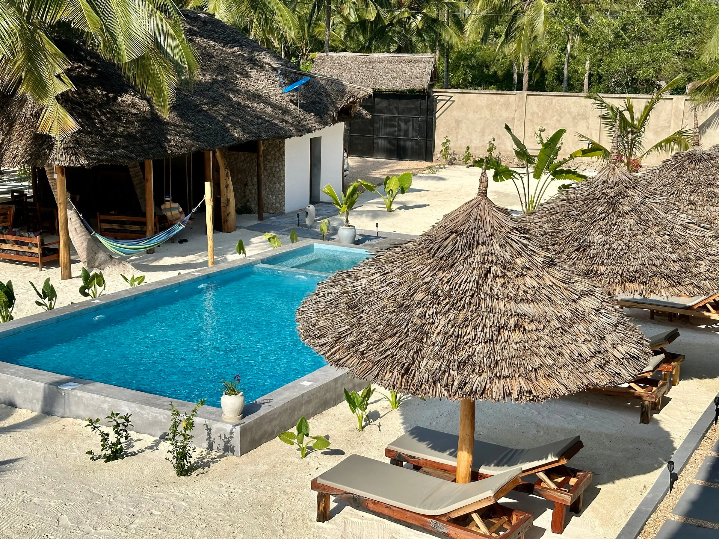 Wooden sun loungers and a thatched umbrella beside the long blue swimming pool