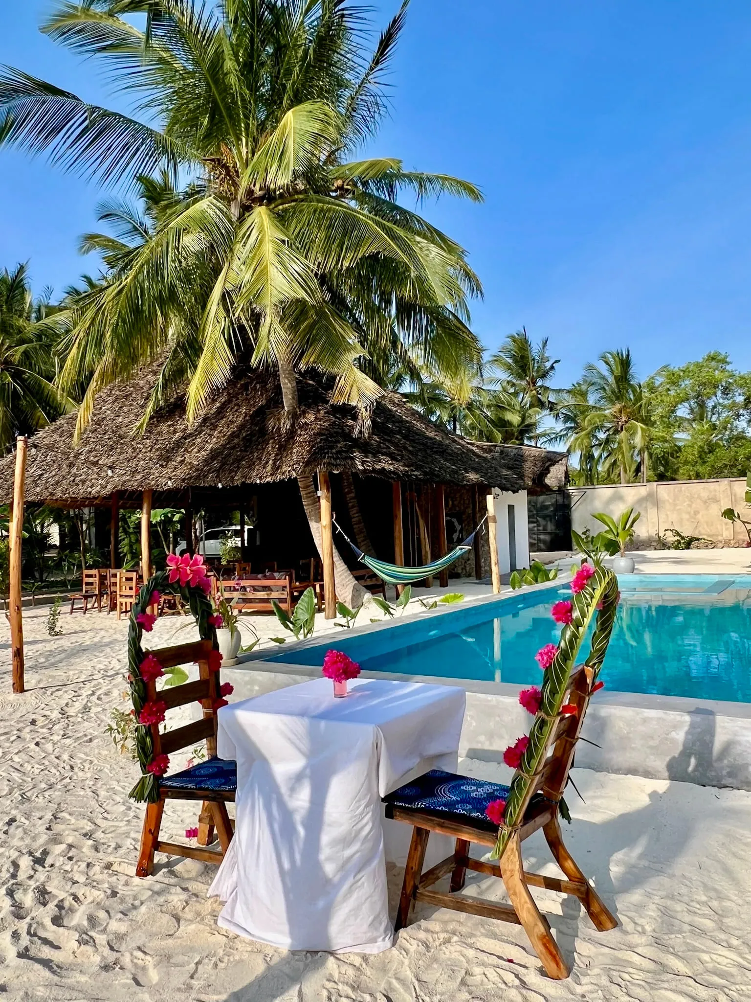 A table for two set with white linen and flowers at the edge of the pool