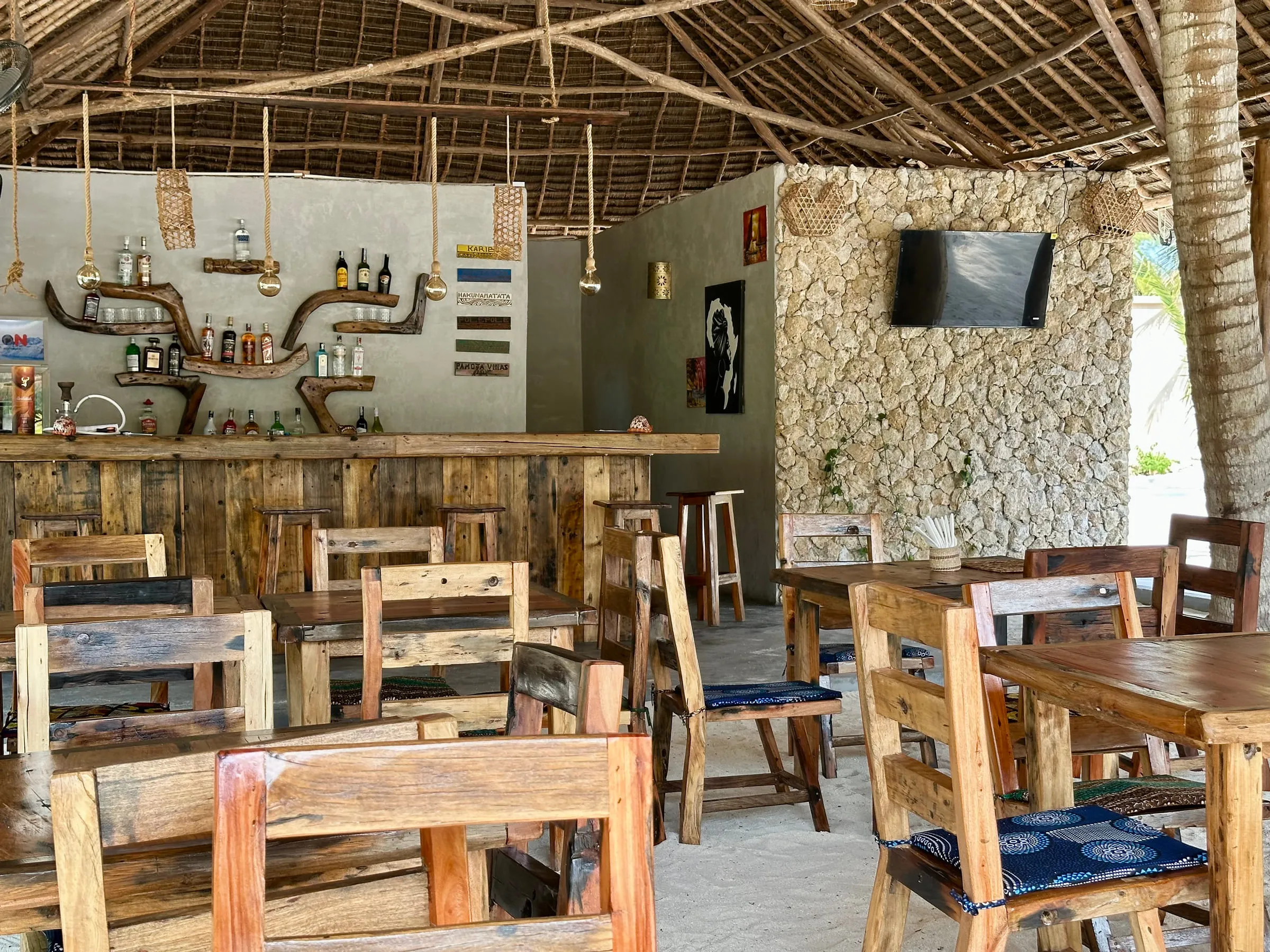 The open-sided restaurant with heavy timber tables, a stone bar and a high makuti roof
