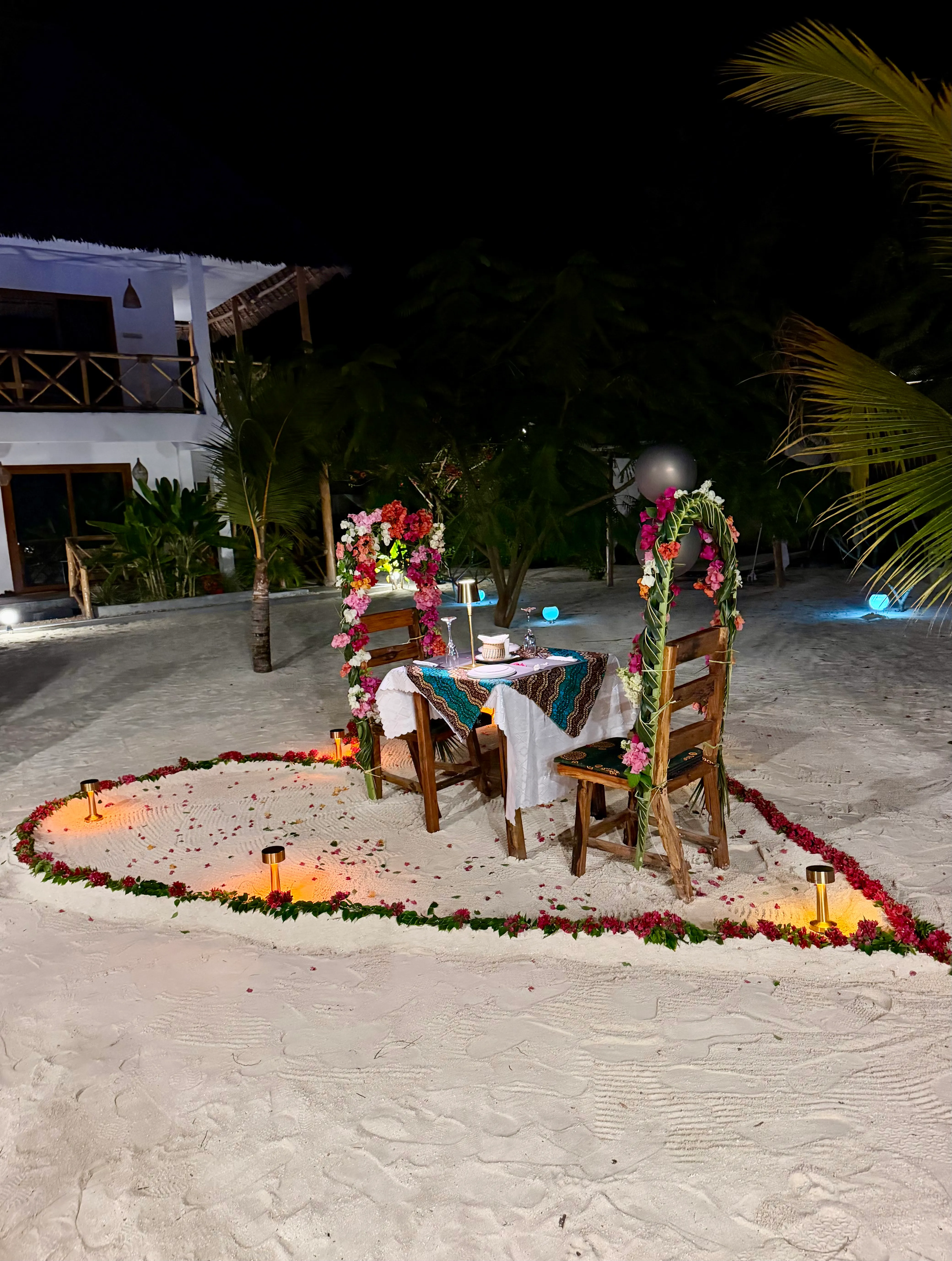 A table for two set with white linen and flowers at the edge of the swimming pool