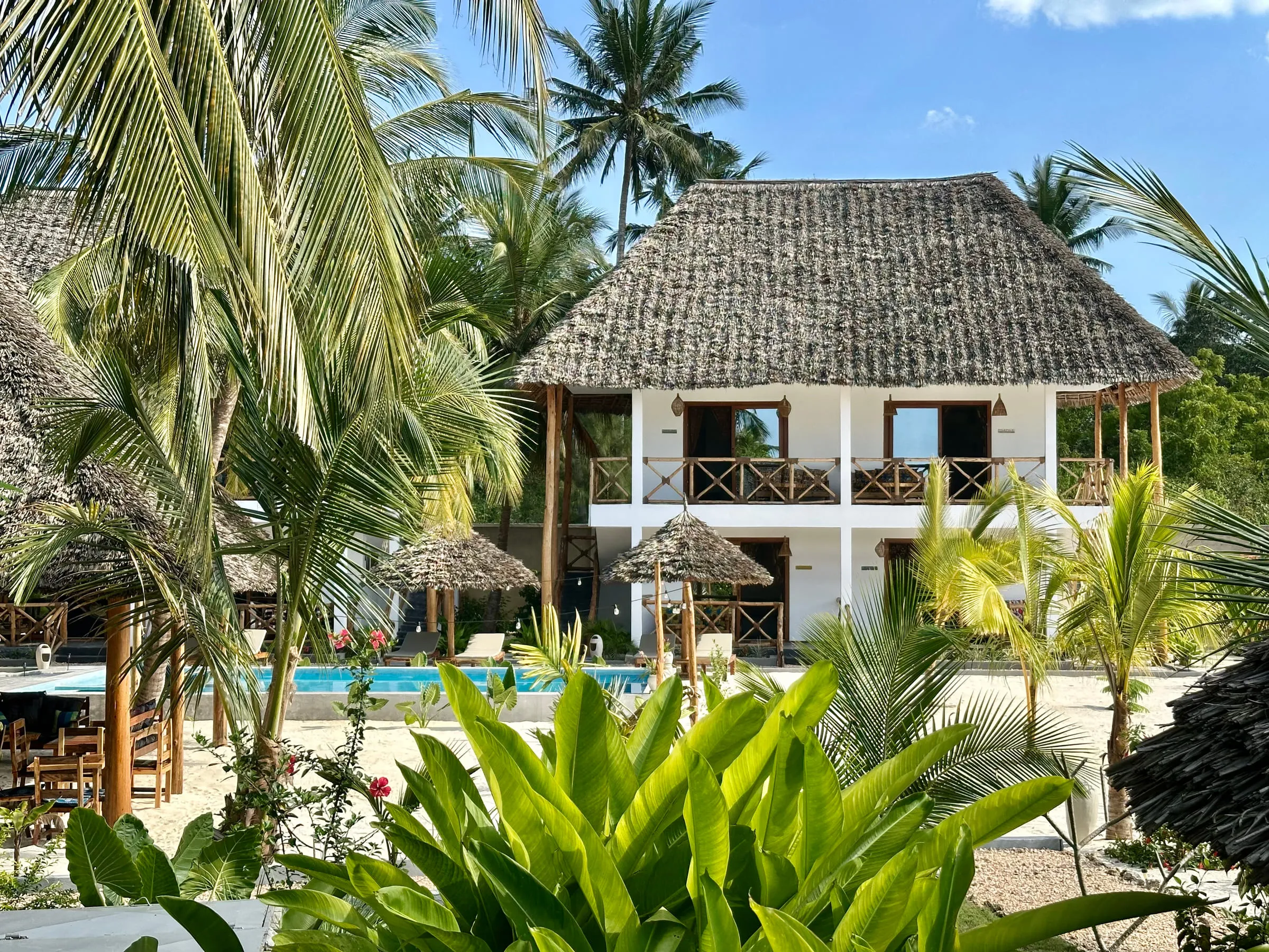 The whitewashed villa with its thatched roof seen through banana leaves and tropical planting